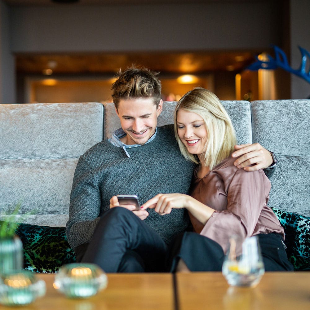 Ein Pärchen nutzt die Digitale Gästemappe von Gastfreund auf einem Smartphones in der Lobby des Hotels