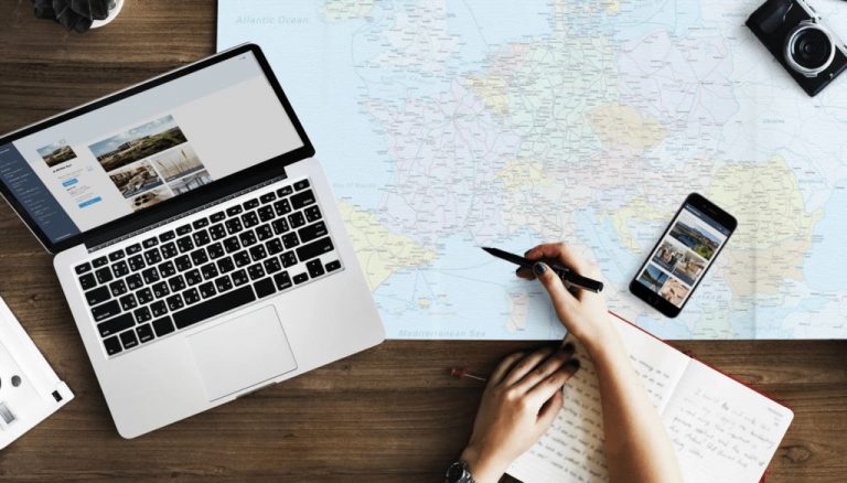 Ein Schreibtisch mit Laptop, Reisekarte und Digitaler Gästemappe von Gastfreund auf einem Smartphone