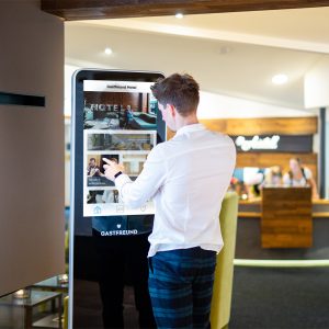 Ein Mann der das Touchscreen-Kiosk von Gastfreund als digitalen Infopoint neben der Rezeption nutzt