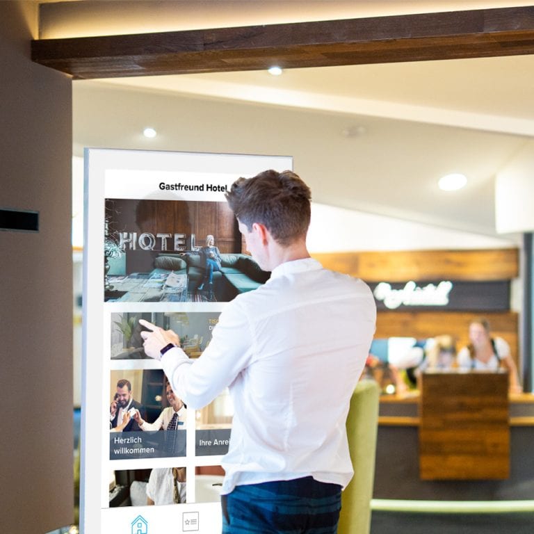 Ein Mann der das Touchscreen-Kiosk von Gastfreund als digitalen Infopoint neben der Rezeption nutzt