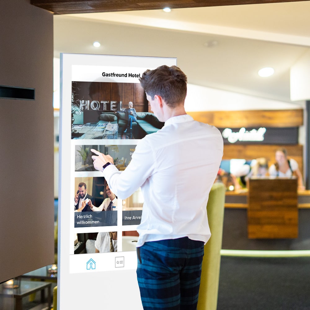 Ein Mann der das Touchscreen-Kiosk von Gastfreund als digitalen Infopoint neben der Rezeption nutzt