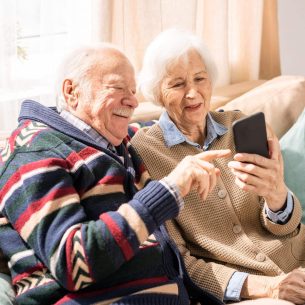 Portrait of adorable senior couple using smartphone together video chatting with family at home, copy space